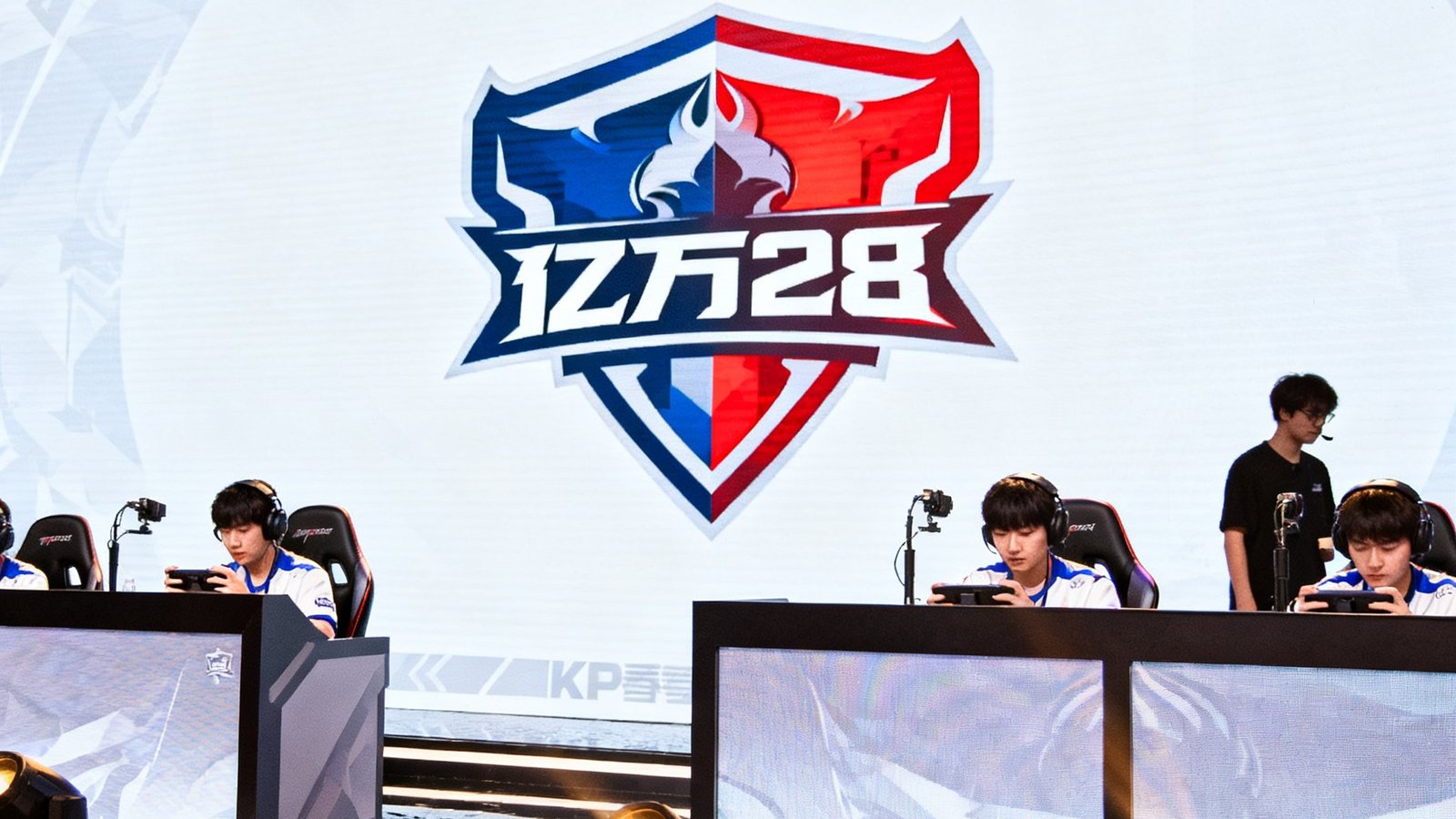 KPL春季赛现场，舞台大屏显示亿万28 logo，选手正在比赛